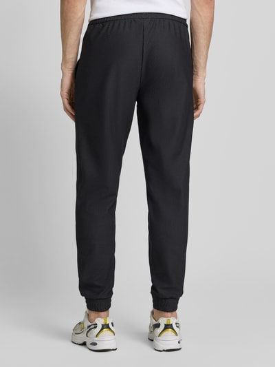 Mężczyzna nosi Regular Fit Sweatpants mit Strukturmuster od EA7 Emporio Armani, elastyczny materiał, kieszenie, czarny kolor, fakturowana powierzchnia, krój regular fit, widok całej sylwetki od tyłu.