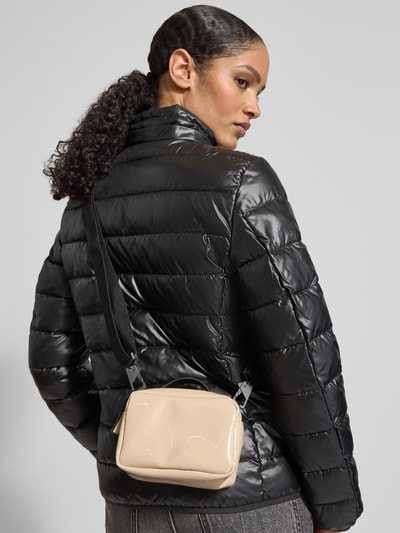 Frauenmodel trägt Handtasche mit Reißverschluss Modell 'BOX BAG MICRO' von RAINS in Beige, glänzende Oberfläche, verstellbarer schwarzer Schulterriemen, Ganzkörperansicht Rückansicht.