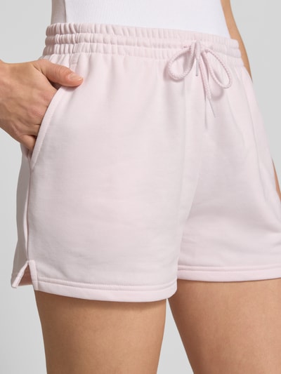 Frauenmodel trägt Straight Fit Shorts mit Tunnelzug Modell 'French' von New Balance aus Baumwoll-Mix, zartrosa, Nahaufnahme Oberschenkel.