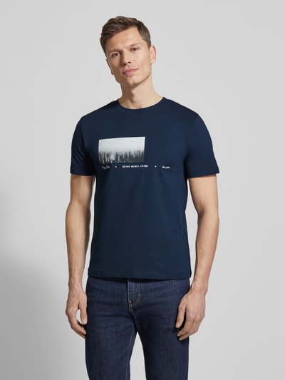 Männermodel trägt Regular Fit T-Shirt aus reiner Baumwolle von Tom Tailor Denim in Dunkelblau mit Foto- und Schriftzug-Print, Ganzkörperansicht von vorne.