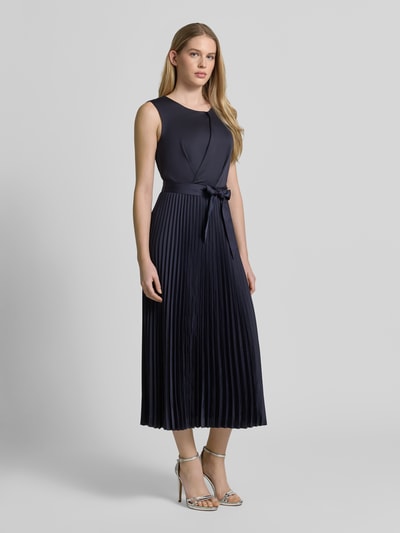 Modelka nosi Cocktailkleid mit Plisseefalten von Vera Mont, granatowy kolor, krój slim fit, długość midi, okrągły dekolt, drapowania, pasek w talii, plisy, zamek z tyłu, długość pleców w rozmiarze 36: 126 cm, szerokość w rozmiarze 36: 30 cm, widok całej sylwetki z przodu