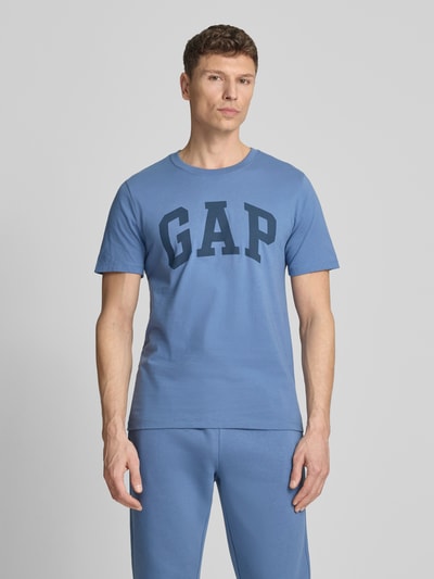 Männermodel trägt T-Shirt mit Logo und Rundhalsausschnitt von GAP in Blau, aus reiner Baumwolle, Regular-Fit, Ganzkörperansicht von vorne. Rückenlänge 72 cm bei Größe M.