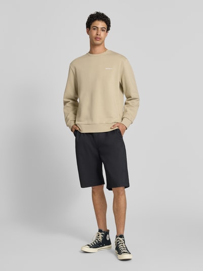Männermodel trägt Sweatshirt mit Rundhalsausschnitt und Label-Stitching von Carhartt Work In Progress in Beige, Baumwoll-Elasthan-Mix, Regular-Fit, Ganzkörperansicht von vorne.
