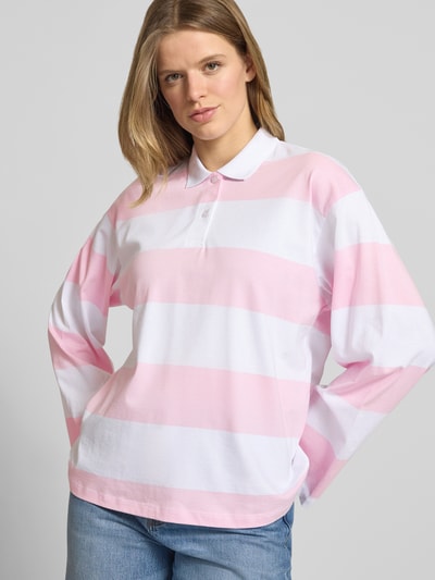 Frauenmodel trägt Relaxed Fit Poloshirt aus reiner Baumwolle Modell 'VILMA' von JJXX, rosa-weiß gestreift, Langarm, Nahaufnahme Oberkörper.