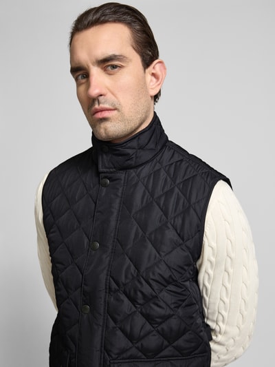 Męski model nosi Regular Fit Steppweste mit Stehkragen od Barbour, gładka czerń, stebnowane pikowanie, stójka, zapięcie kryty suwak i napy, przeszywane kieszenie z patką, kieszeń wewnętrzna na suwak, label stitching, widok z przodu, zbliżenie na górę ciała.