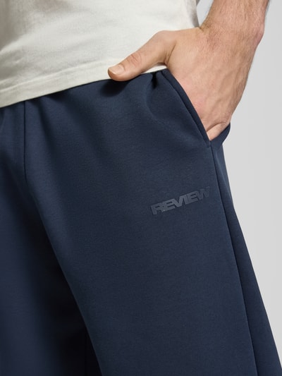 Männermodel trägt Sweatpants aus Baumwoll-Mix von REVIEW in Dunkelblau mit Seitentaschen und Label-Detail, Nahaufnahme Oberschenkel.