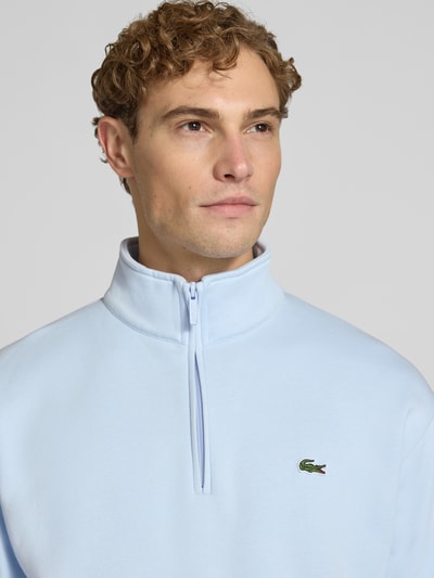 Männermodel trägt hellblauen Regular Fit Troyer aus Baumwoll-Mix von Lacoste, glatte Textur, Nahaufnahme Oberkörper, Herren Troyer von Lacoste.