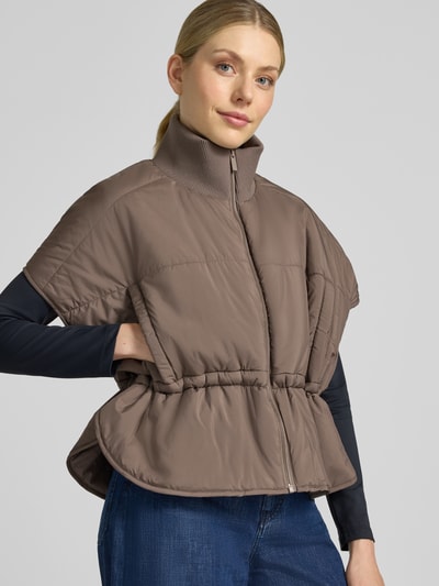 Modelka kobieca nosi Steppweste mit Stehkragen Modell 'Vanjah' von someday, kolor brązowy, luźny krój relaxed fit, zamek błyskawiczny, stójka, długość tyłu w rozmiarze 36: 58 cm, szerokość ramion w rozmiarze 36: 75 cm, szerokość w biuście w rozmiarze 36: 59 cm, widoczne miękkie przeszycia, gładka tekstura, pełen kadr od przodu.