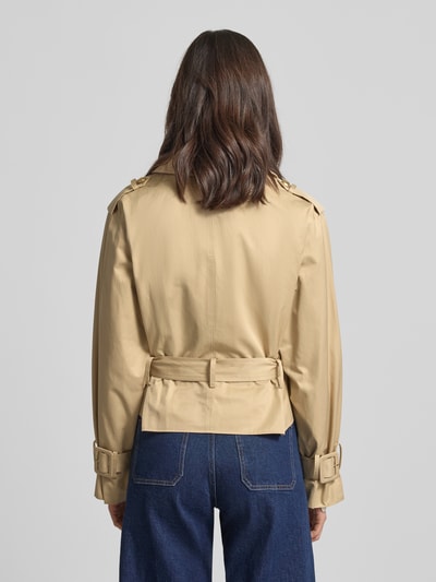 Frauenmodel trägt Cropped Trenchcoat mit Reverskragen Modell 'Fatou' von Guess aus Baumwoll-Mix in Beige, Ganzkörperansicht Rückansicht. Taillierte Passform, Doppelreihe Knopfleiste, Stoffgürtel, Rückenlänge 53 cm, Schulterbreite 41 cm, Brustweite 40 cm, Ärmellänge 58 cm.