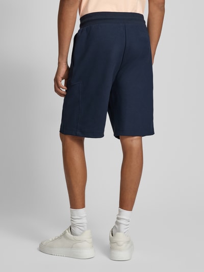 Männermodel trägt dunkelblaue Shorts mit Eingrifftaschen Modell 'Joseignacio' von JOOP! Collection, lockere Passform, Baumwoll-Mix, Ganzkörperansicht Rückansicht.