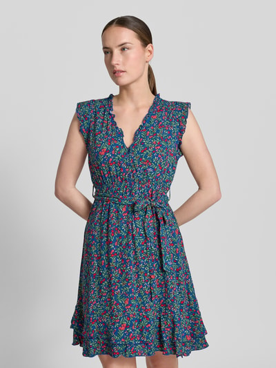 Frauenmodel trägt Minikleid aus Viskose mit Bindegürtel von Apricot, taillierter Schnitt, V-Ausschnitt mit Rüschen, florales Muster, Ganzkörperansicht von vorne.