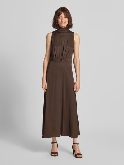 Frauenmodel trägt Maxikleid mit Stehkragen und Drapierungen Modell 'AMABEL' von DRYKORN in Braun, A-Linie, Material-Mix, Ganzkörperansicht von vorne.