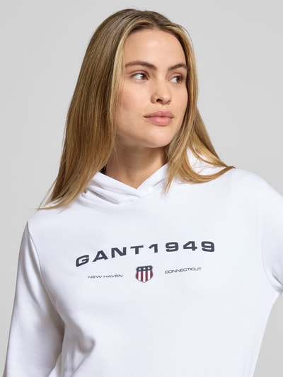 Vrouwenmodel draagt Regular Fit Hoodie met labelprint van Gant, wit katoenmix, labelprint op borst, Nahaufnahme bovenlichaam.