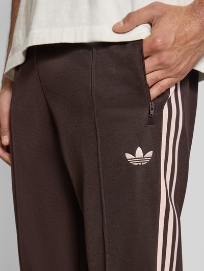 Männermodel trägt Sweatpants mit elastischem Bund von adidas Originals, braun mit rosa Streifen, lockerer schnitt, nahaufnahme oberkörper, katoenmix, label-stitching, ritszakken, achterzak, binnenbeenlengte maat M 75 cm