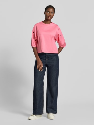 Kobiece model nosi T-Shirt mit 3/4-Arm und Lochstickerei von Marc Cain z bawełny, krój regular fit, okrągły dekolt, długość tyłu w rozmiarze 36: 52 cm, jasnoróżowy, haft angielski, szerokie jeansy, widok całej sylwetki z przodu.