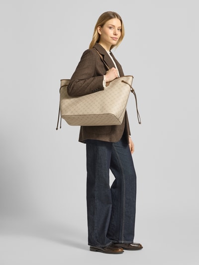 Vrouwenmodel draagt shopper met all-over logoprint, logodetail, schouderbanden, model 'Lara' van JOOP!, lengte 34 cm, breedte 53 cm, diepte 20 cm, bandlengte 56 cm, hoofdvak, voor dames, zijaanzicht