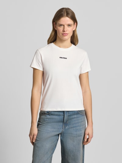 Frauenmodel trägt T-Shirt mit Rundhalsausschnitt und Logo-Stitching von Review aus Baumwoll-Mix mit Stretch-Anteil, körpernaher Schnitt, weiß, Ganzkörperansicht von vorne.
