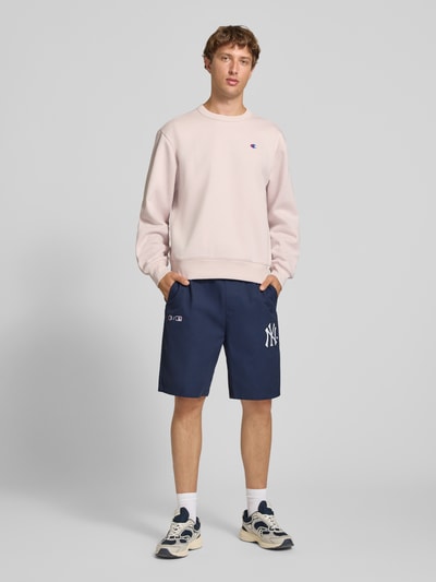 Männermodel trägt Relaxed Fit Shorts aus reiner Baumwolle von Champion, navyblau, elastischer Bund, Logo-Stitching, Ganzkörperansicht von vorne.