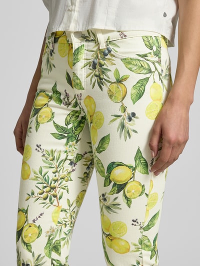 Kobiece modelka nosi Slim Fit Jeans mit floralem Allover-Print od Marc Cain, jasne kolory, cytrynowe i oliwkowe wzory, elastyczna bawełniana mieszanka, pięciokieszeniowy fason, zapięcie na guzik i zamek, szerokość w rozmiarze 36: 38 cm, długość wewnętrzna nogawki w rozmiarze 36: 53 cm, krój slim fit, zbliżenie na biodra i uda, ujęcie z przodu