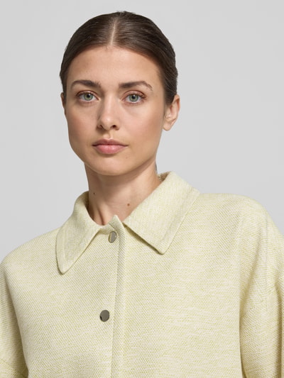 Vrouwenmodel draagt Regular Fit jack met viscose van More & More in lichtgeel met structuurpatroon, knoopsluiting, platte kraag, detailopname bovenlichaam.