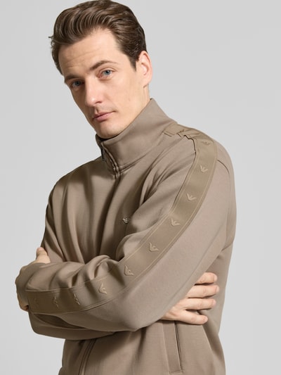 Männermodel trägt Sweatjacke mit Stehkragen und Zweiwege-Reißverschluss von Emporio Armani, Baumwoll-Mix mit Stretch-Anteil, Regular-Fit, Eingrifftaschen, Rückenlänge bei Größe M 66 cm, Ärmellänge 62 cm, Beige-Ton, glatte Struktur, Nahaufnahme Oberkörper.