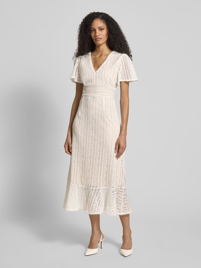 Modelka kobieca nosi Midikleid aus Häkelspitze mit V-Ausschnitt od Apricot, kremowa koronka, krój slim fit, pasek w talii, długość pleców w rozmiarze S: 124 cm, szerokość w rozmiarze S: 40 cm, długość rękawa w rozmiarze S: 24 cm, widok całej sylwetki z przodu.