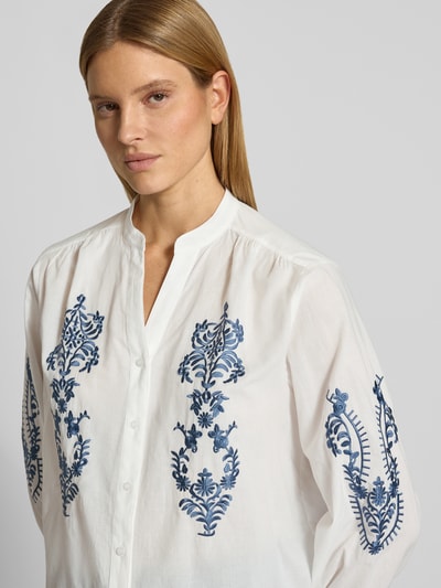 Frauenmodel trägt Regular Fit Bluse mit floralem Stitching Modell 'Februar' von More & More aus Reine Baumwolle, weiß mit blauen Stickereien, Langärmelig, Tunika-Ausschnitt, durchgängige Knopfleiste, elastische Ärmelabschlüsse, Rückenlänge bei Größe 36: 60 cm, Ärmellänge: 60 cm, Nahaufnahme Oberkörper.