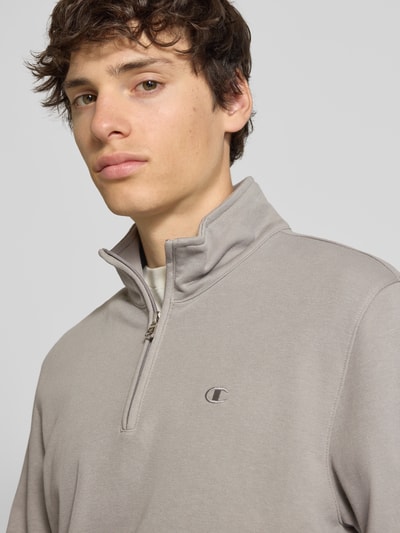 Männermodel trägt Sweatshirt mit Stehkragen und Reißverschluss von CHAMPION in Beige, Baumwoll-Mix, Label-Stitching, Nahaufnahme Oberkörper.