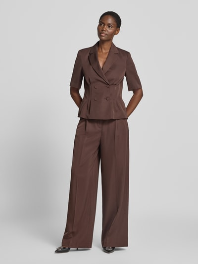 Modelka kobieca ma na sobie spodnie z zakładkami w pasie Wide Leg Bundfaltenhose mit Gesäßtaschen von Christian Berg Cocktail, Mieszanka materiałów z dodatkiem lyocellu, efekt błyszczący, kieszenie z tyłu, kolor brązowy, szerokość w rozmiarze 36: 36 cm, długość wewnętrzna nogawki w rozmiarze 36: 82 cm, Ganzkörperansicht von vorne.
