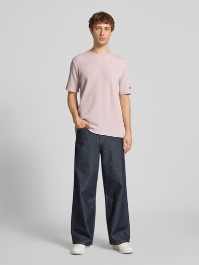 Männermodel trägt T-Shirt mit Strukturmuster und Label-Stitchings von CHAMPION in Hellrosa, kombiniert mit Jeans, Baumwoll-Mix, Regular-Fit, Rückenlänge bei Größe M 68 cm, Ganzkörperansicht von vorne.