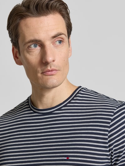 Männermodel trägt Regular Fit T-Shirt aus reiner Baumwolle von Tommy Hilfiger mit Allover-Streifen und Logo, Nahaufnahme Oberkörper.