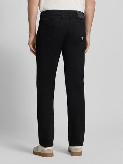 Männermodel trägt Slim Fit Jeans im 5-Pocket-Design Modell 'ANGELS' von Guess in Schwarz, Baumwoll-Elasthan-Mix, Ganzkörperansicht Rückansicht.