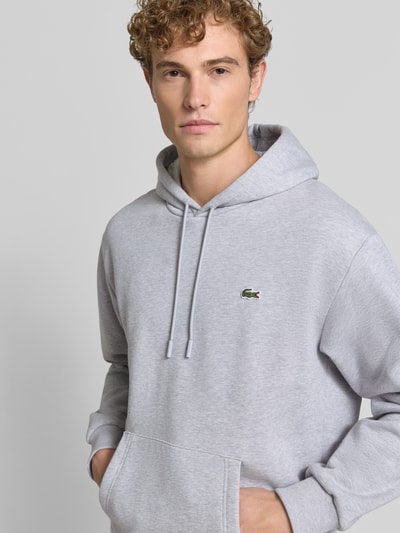 Męski model nosi Relaxed Fit Hoodie aus Baumwoll-Mix od Lacoste w jasnoszarym kolorze, gładka tekstura, bluza z kapturem, Nahaufnahme Oberkörper, Herren Sweatshirt von Lacoste