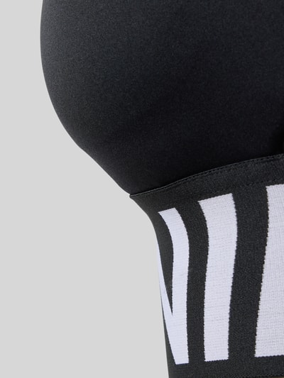 Frauenmodel trägt Racerback-Bustier mit Cut Out und Label-Details von NIKE TRAINING, Material-Mix mit Stretch-Anteil, körpernahe Passform, Nahaufnahme Oberkörper.