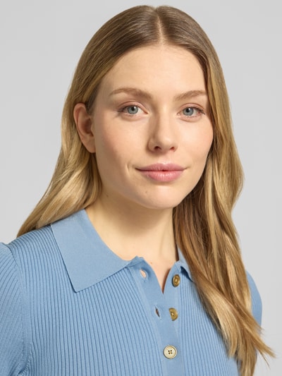 Frauenmodel trägt Midikleid aus Viskose mit Polokragen und Knopfleiste von MICHAEL Michael Kors in A-Linie, feine Rippenstruktur, Nahaufnahme Oberkörper.