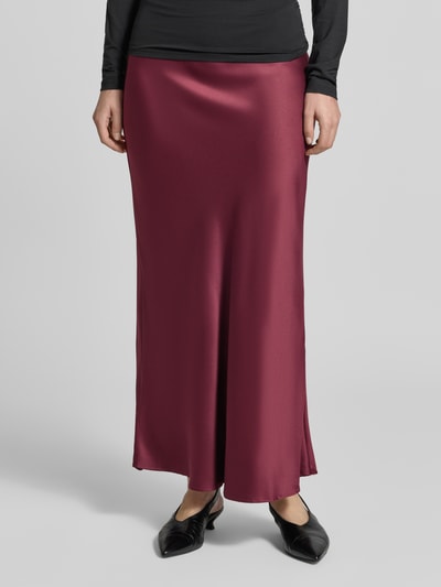 Kobiece model prezentuje spódnicę maxi z połyskującą, bordową tkaniną, model 'MERLE' od VERO MODA, zbliżenie dolnej części ciała.