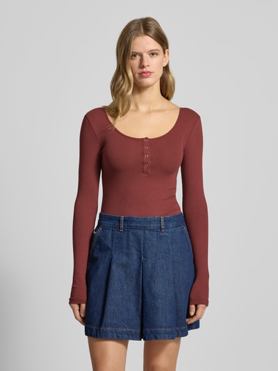 Modelka kobieca nosi Slim Fit Langarmshirt aus Baumwoll-Mix Modell 'KITTE' od Pieces, w kolorze bordowym, prążkowana faktura, paski, z krótką listwą guzikową, widok całej sylwetki z przodu.