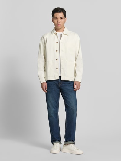 Męski model nosi Regular Fit Jeansjacke aus Bio-Baumwoll-Mix Modell 'HOTEL AMOUR' von SELECTED HOMME w kolorze ecru, jednolita faktura, długie rękawy, guziki, kieszenie; perspektywa: całe ciało z przodu.