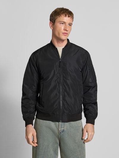 Męski model nosi Regular Fit Bluzon z college’owym kołnierzem Model 'JOSHUA' od Only & Sons, jednokolorowy, długi rękaw, zamek błyskawiczny, prążkowane wykończenia, wpuszczane kieszenie, kieszeń na rękawie, widok całej sylwetki z przodu.