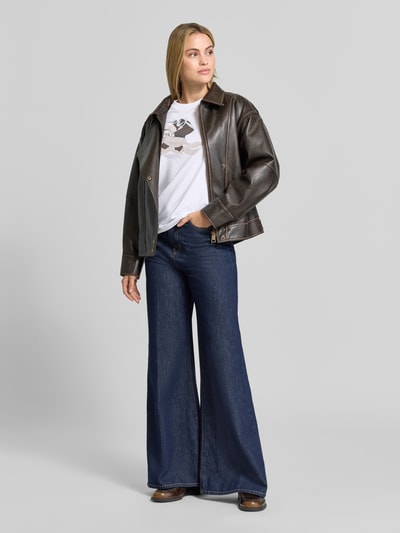 Frauenmodel trägt T-Shirt mit Label-Print von COMMA im elastischen Baumwoll-Mix, weiß, kombiniert mit blauer Schlagjeans, Ganzkörperansicht von vorne.