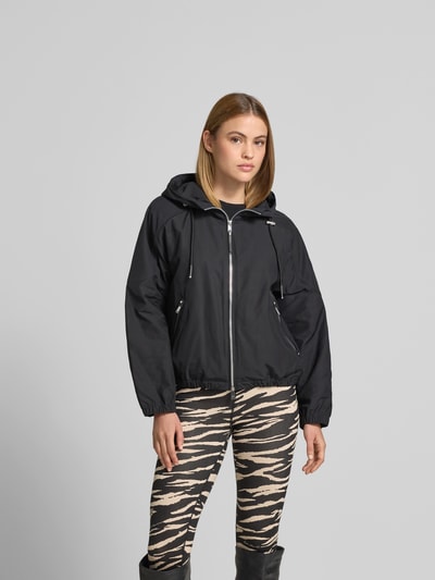 Frauenmodel trägt Jacke mit Zweiwege-Reißverschluss von Moose Knuckles, schwarz, Kapuze mit Tunnelzug, Relaxed-Fit, Eingrifftaschen mit Reißverschluss, Rückenlänge 56 cm, Brustweite 56 cm, Ärmellänge 44 cm, Ganzkörperansicht von vorne.