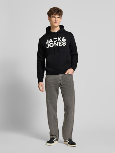 Männermodel trägt Hoodie mit Label-Print und Känguru-Tasche von Jack & Jones in Schwarz, Baumwoll-Mix, Regular Fit, Ganzkörperansicht von vorne.