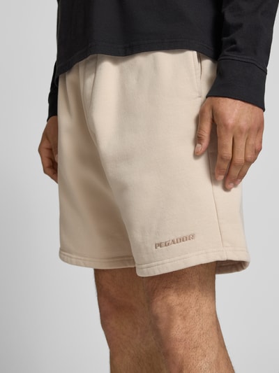 Männermodel trägt Regular Fit Shorts mit Logo-Stitching von Pegador aus Baumwoll-Mix, beige, elastischer Bund, Nahaufnahme Oberschenkel
