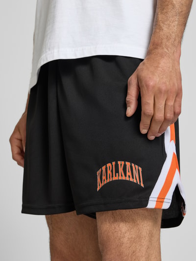 Männermodel trägt Regular Fit Shorts mit Logo-Print von KARL KANI, Schwarz mit Strukturmuster, elastischer Bund, Nahaufnahme Oberschenkel.