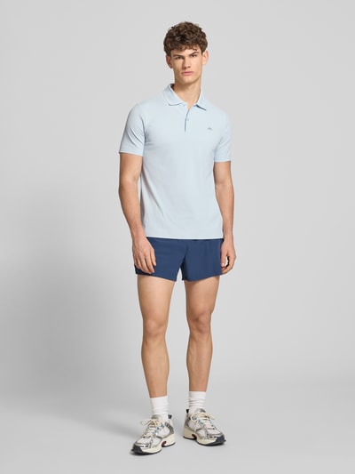 Mężczyzna nosi Slim Fit Poloshirt mit Logo Modell 'EDMOND' od Ellesse, jasnoniebieski, materiał ze streczem, krój slim fit, na guziki, całkowity widok z przodu. Szerokość w rozmiarze M: 63 cm.