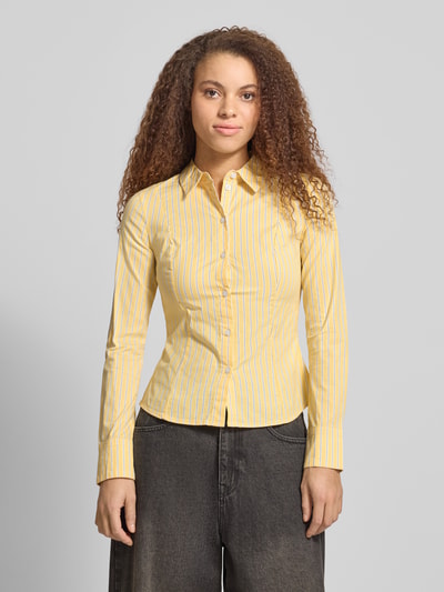 Modelka kobieca nosi Fitted Hemdbluse mit Hemdblusenkragen od Review, elastyczna bawełniana tkanina, krój fitted, żółte i białe paski, długie rękawy, sportowe mankiety, pełna długość guzików, widok całej sylwetki z przodu.