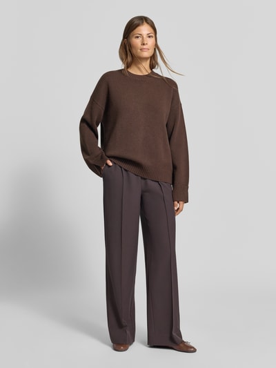 Frauenmodel trägt Wide Fit Sweatpants mit Viskose-Anteil von MYON, braun, strukturierter Stoff, Zierfalten, Ganzkörperansicht von vorne.