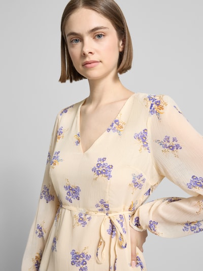 Frauenmodel trägt Minikleid aus Chiffon Modell 'MIRIAM-FUSINA' von Only mit floralem Allover-Muster, V-Ausschnitt, Taillengürtel, langarm, Transparenz in Crème und Lila, Materialverarbeitung: Chiffon, Nahaufnahme Oberkörper.