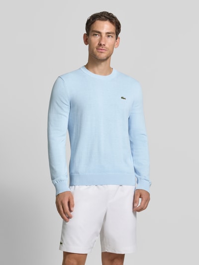 Männermodel trägt hellblauen Regular Fit Pullover aus Baumwoll-Mix von Lacoste, dezentes Logo, glatte Textur, Ganzkörperansicht von vorne. Herren Pullover von Lacoste