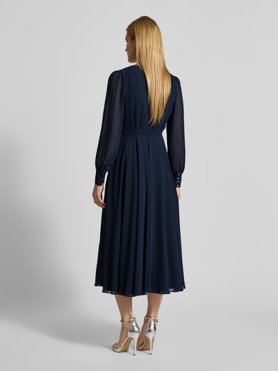 Frauenmodel trägt Regular Fit Midikleid mit Taillenband von Christian Berg Cocktail, Dunkelblau, Chiffon, Langärmelig, semitransparent, Falten-Optik, Nahtreißverschluss, taillierte Passform, Blickdichter Unterrock, Ganzkörperansicht Rückansicht.